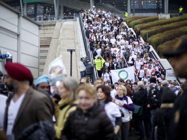 A large rally of protesters, many wearing the same t-shirt, coming down a set of stairs. One is holding a Friends of the Earth banner.