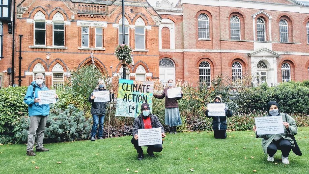 People stand socially distanced holding signs demanding climate action