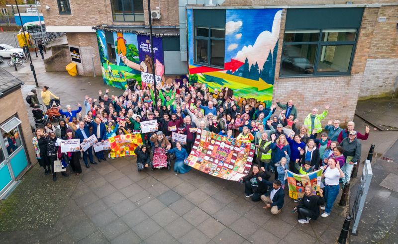 A massive group of people looking joyful holding up their creative quilts. They're outside