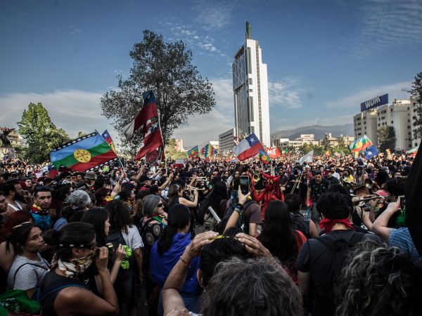 A large protest happening, which looks like a very busy crowd. A few people are waving a Chilean flag and a few are holding their phones up.