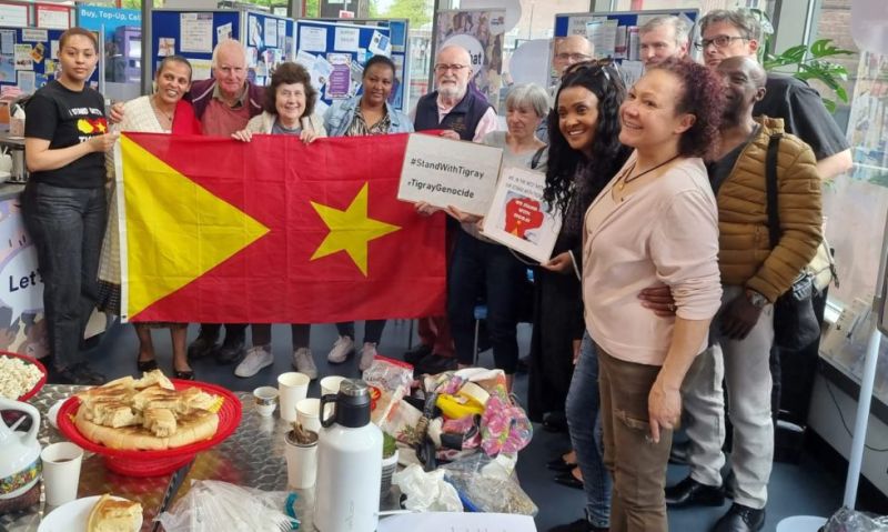 A group photo of people holding a Tigray flag and signs which read #StandWithTigray