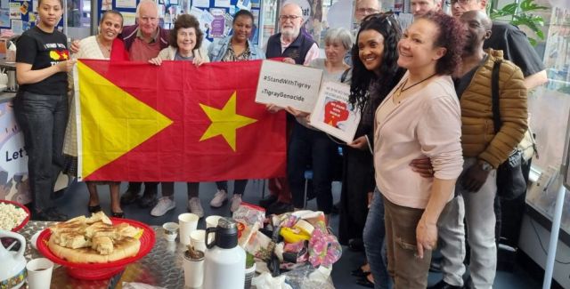 A group photo of people holding a Tigray flag and signs which read #StandWithTigray