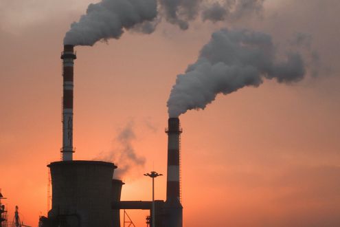A photo of the top of a factory emitting smoke at dusk