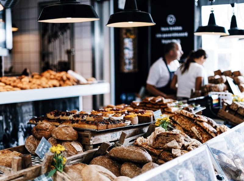 Plastic-free unwrapped bread and pastries in bread shop with 2 assistants in background.