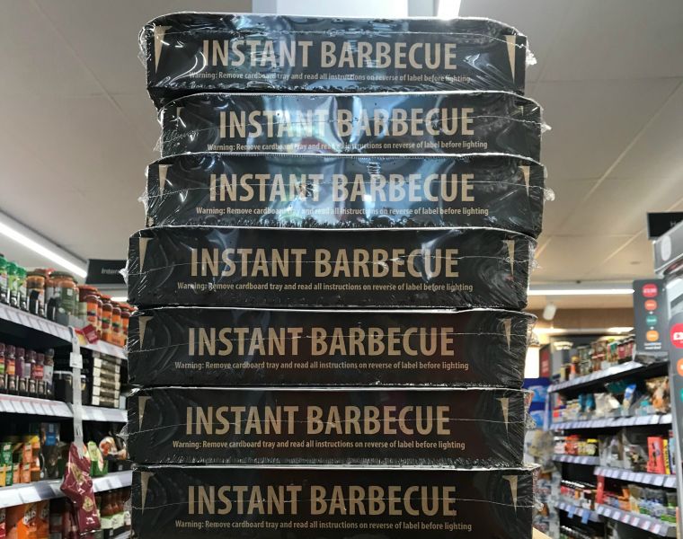 7 single-use plastic-wrapped barbecue trays stacked in supermarket