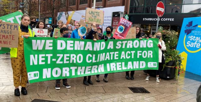 Protesters outside in Belfast City Centre holding a sign up saying 'We demand a strong net-zero climate act for Northern Ireland' 