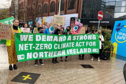 Protesters outside in Belfast City Centre holding a sign up saying 'We demand a strong net-zero climate act for Northern Ireland' 