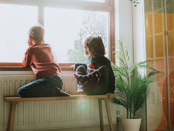 Two children on a bench next to a radiator looking out of a window