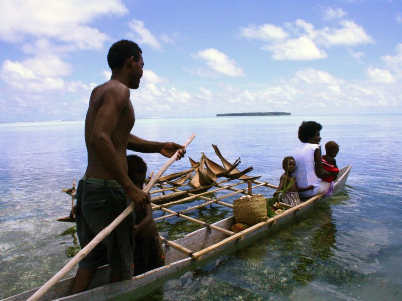 A man rows his family to an unknown destination on a long narrow boat in the waters of Papa New Guinea