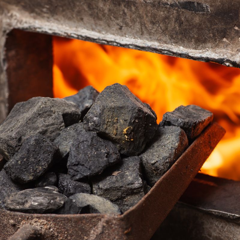 A scoop of coal being fed into a lit furnace
