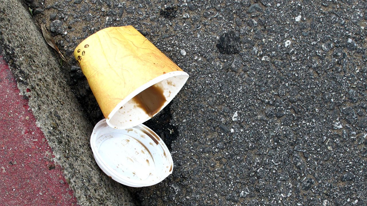 A discarded coffee cup lies on the curb with the remnants of the drink spilling out