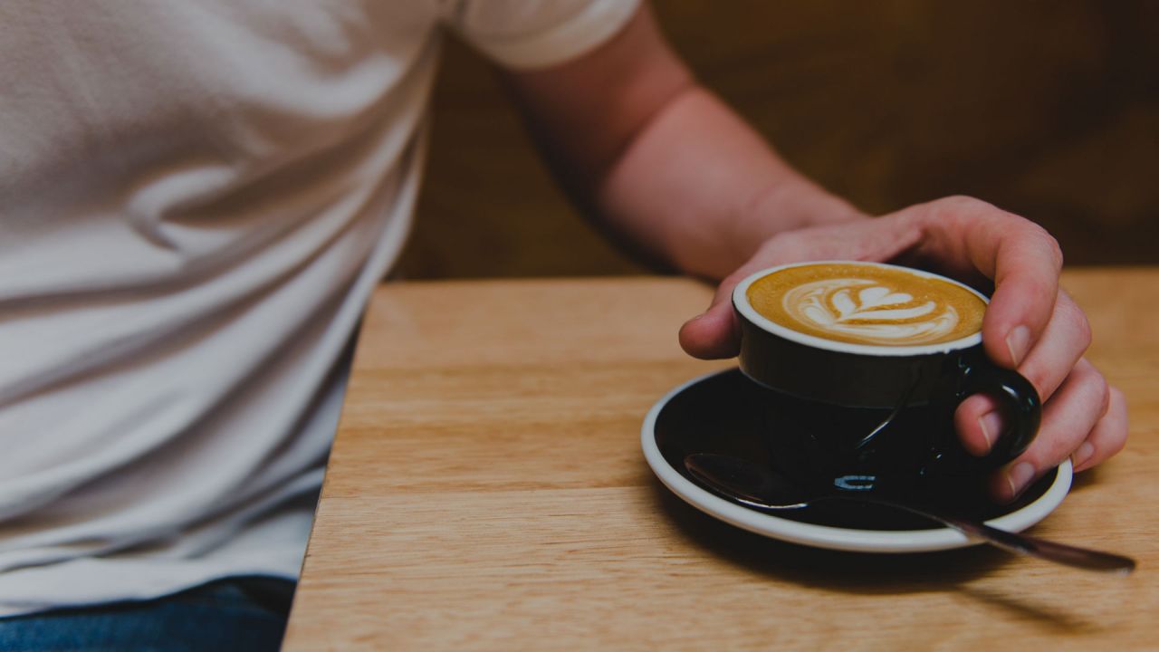 A man in a white t-shirt enjoying a cappuccino