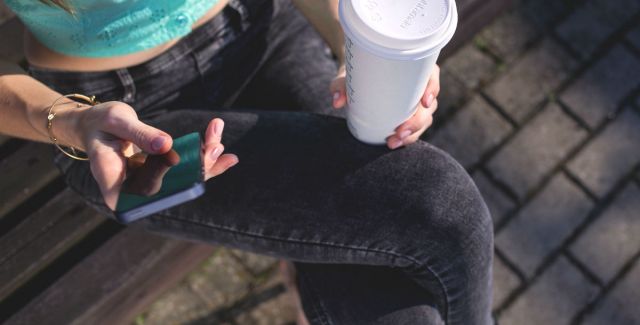 A woman texting while holding a takeaway coffee cup