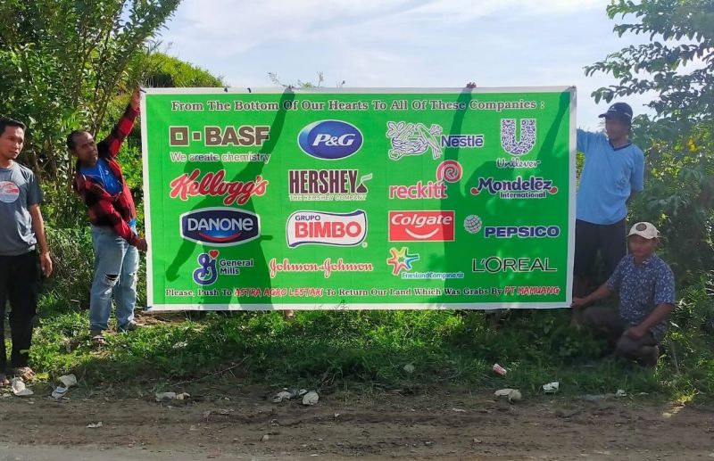 Four men holding a large a banner calling on various companies to push AAL to return their land