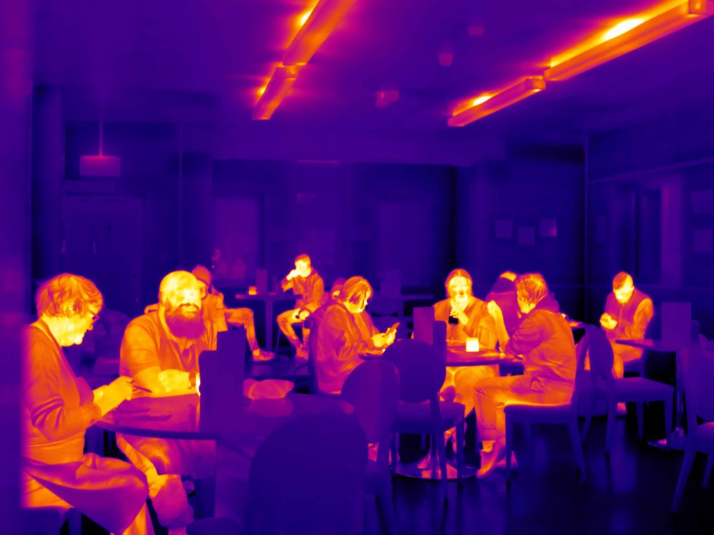 Thermal image of people sat around tables talking and eating together.
