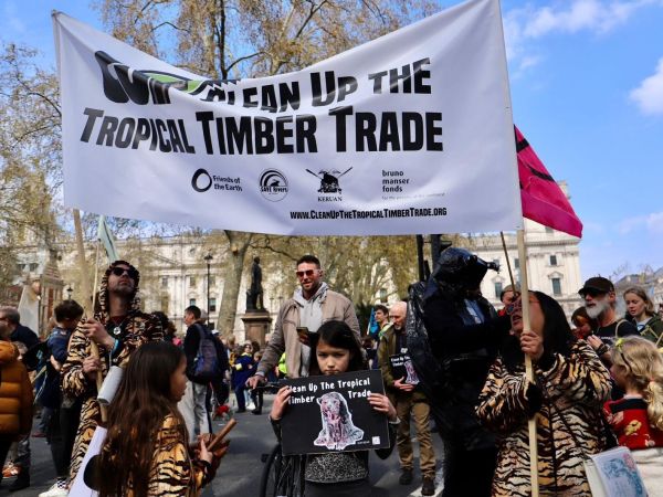 Group members at a march holding a banner and sign reading "Clean Up the Tropical Timber Trade"