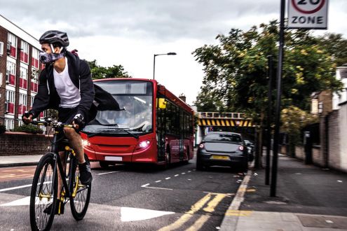 Cyclist wearing breathing mask, on road with bus and cars