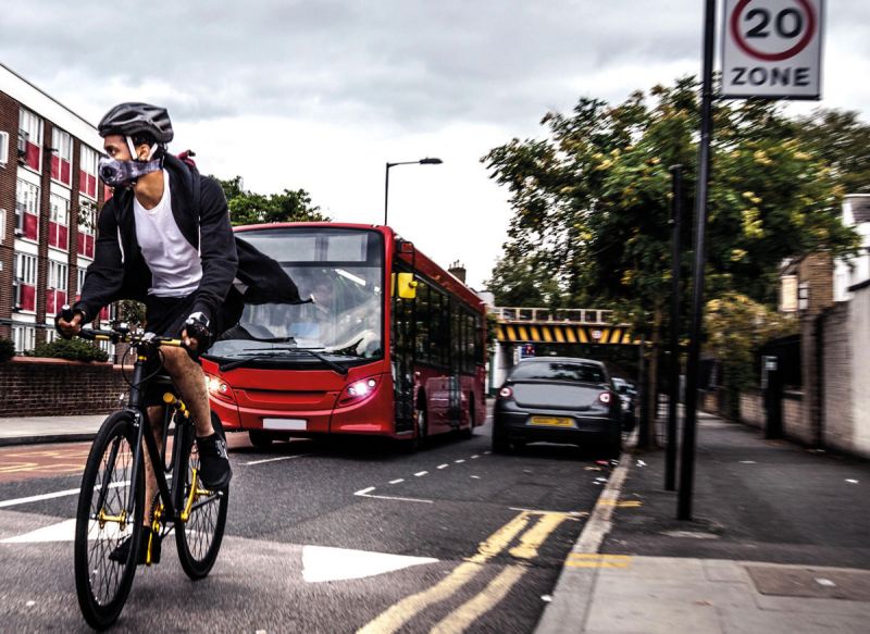 Cyclist wearing breathing mask, on road with bus and cars