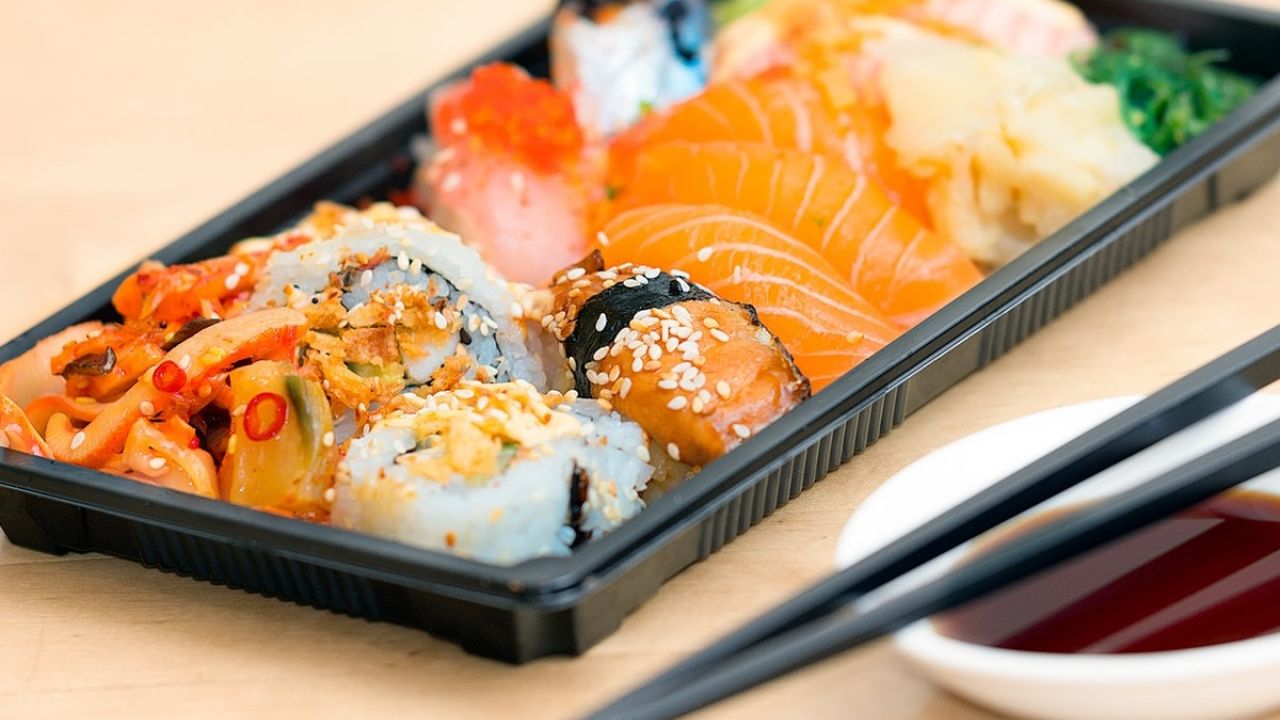 A black plastic food tray containing a sushi ready meal, with chopsticks
