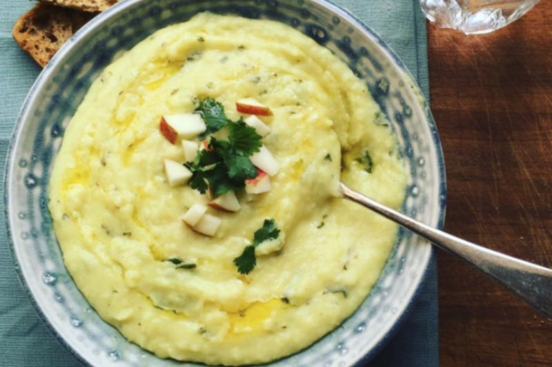 A bowl of spiced parsnip soup with a garnish of apple, parsley and ginger, in a blue bowl