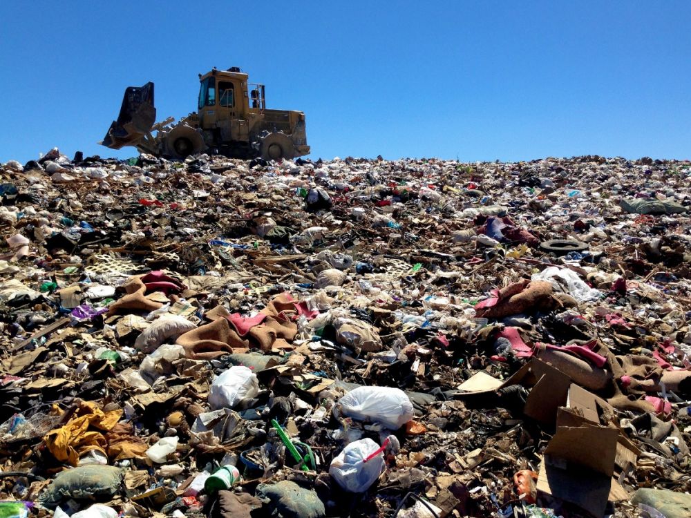 A digger moves through a pile of rubbish at a landfill site