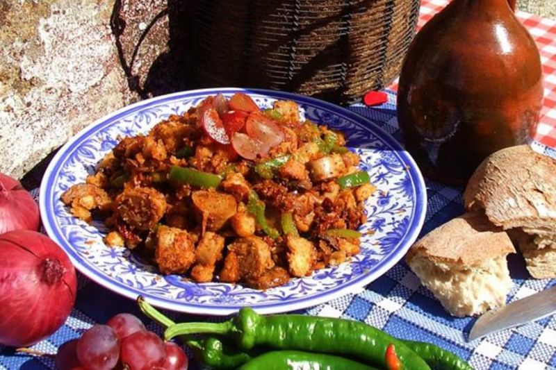 Migas - bowl of traditional Spanish recipe bread salad on table. Onions, chili peppers and grapes around the dish.