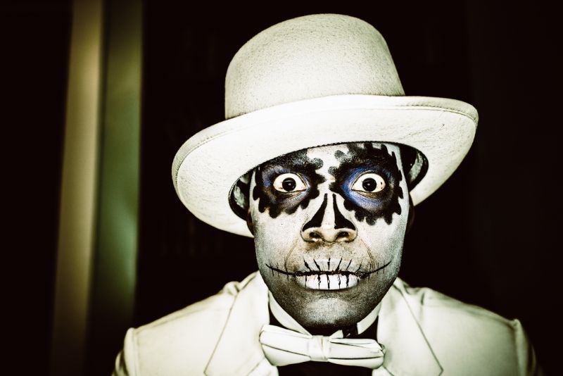 Close-up of a man in a Day of The Dead outfit in white bow tie, hat and coat with ghoulish face paint