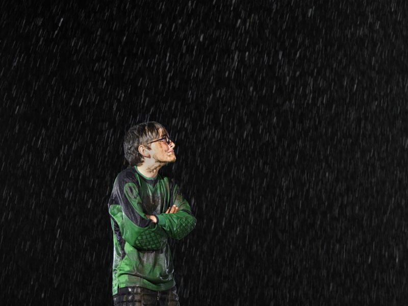A boy wearing a dirty football kit in the rain