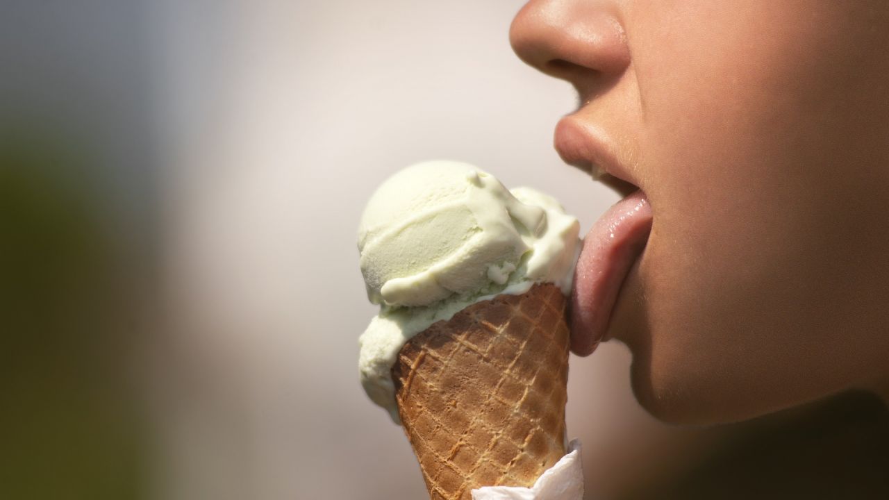 A woman licking ice cream from a cone