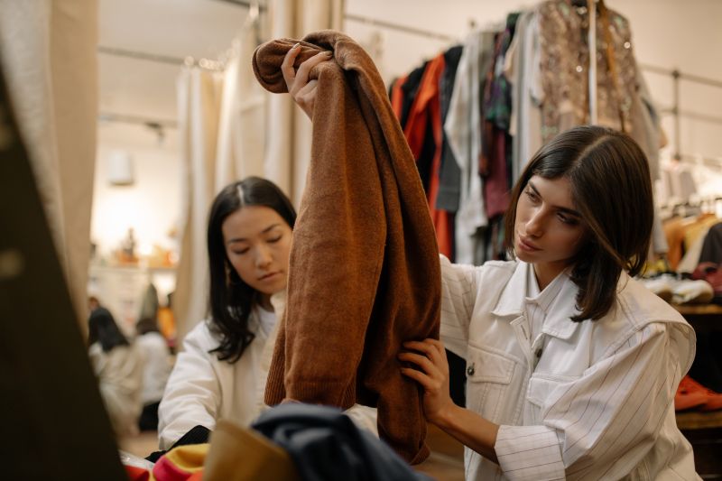 Two women in a thrift store looking at a brown fleece