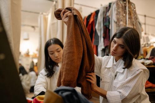 Two women in a thrift store looking at a brown fleece