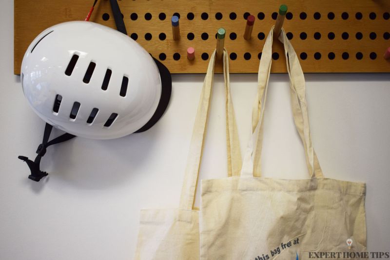 Canvas bags hanging on wooden peg board next to cycle helmet