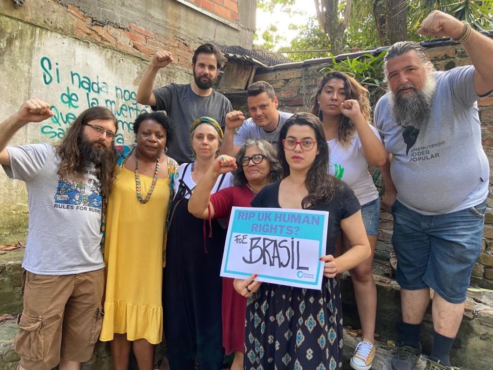A group of people from FOE Brazil stand with their fists raised and a sign saying "RIP UK human rights?"