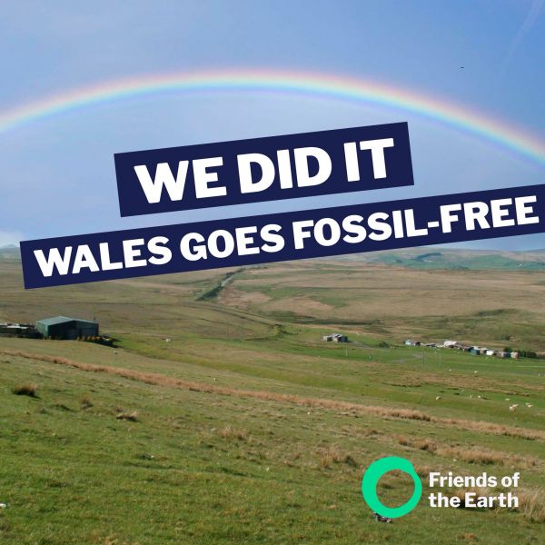 Rainbow over green flatlands with large text saying We Did It - Wales goes fossil free