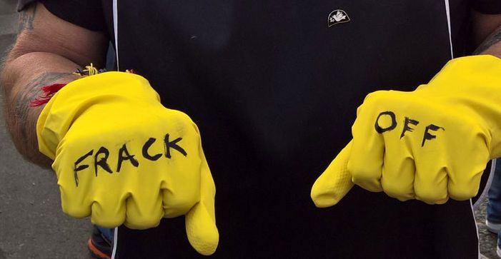 Photo of fists in yellow rubber gloves with "frack off" written on them
