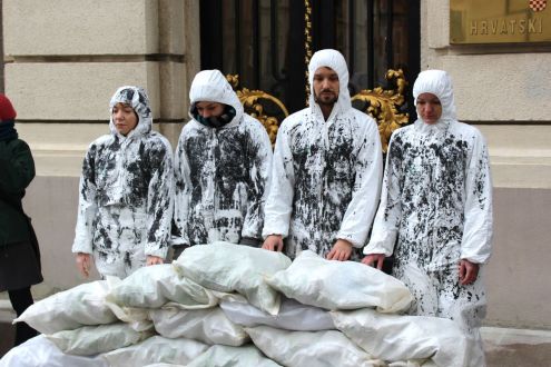 4 members of Friends of the Earth Croatia wearing oil-stained overalls standing outside a government building to protest against drilling in the Adriatic Sea