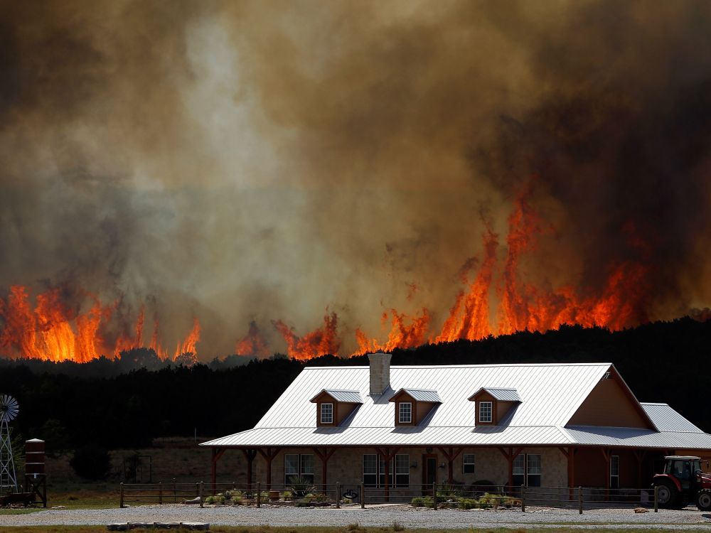 Wildfires appear over a hill behind a house in Texas