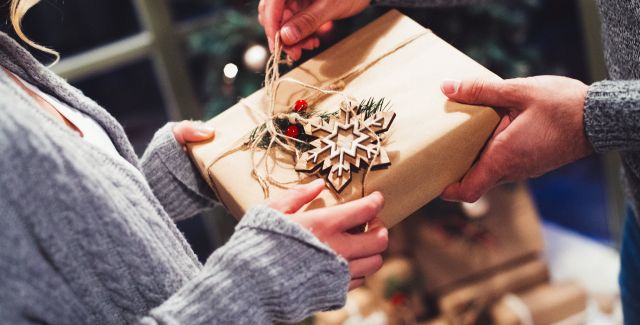 A couple exchanging a gift wrapped up in beautiful brown paper with a wooden ornament attached