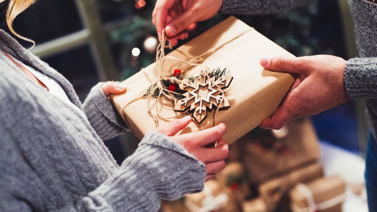 A couple exchanging a gift wrapped up in beautiful brown paper with a wooden ornament attached