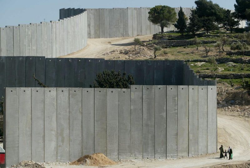 A Palestinian family (shown very small) passes by a section of the controversial Israeli “security barrier” in Abu Dis, West Bank.