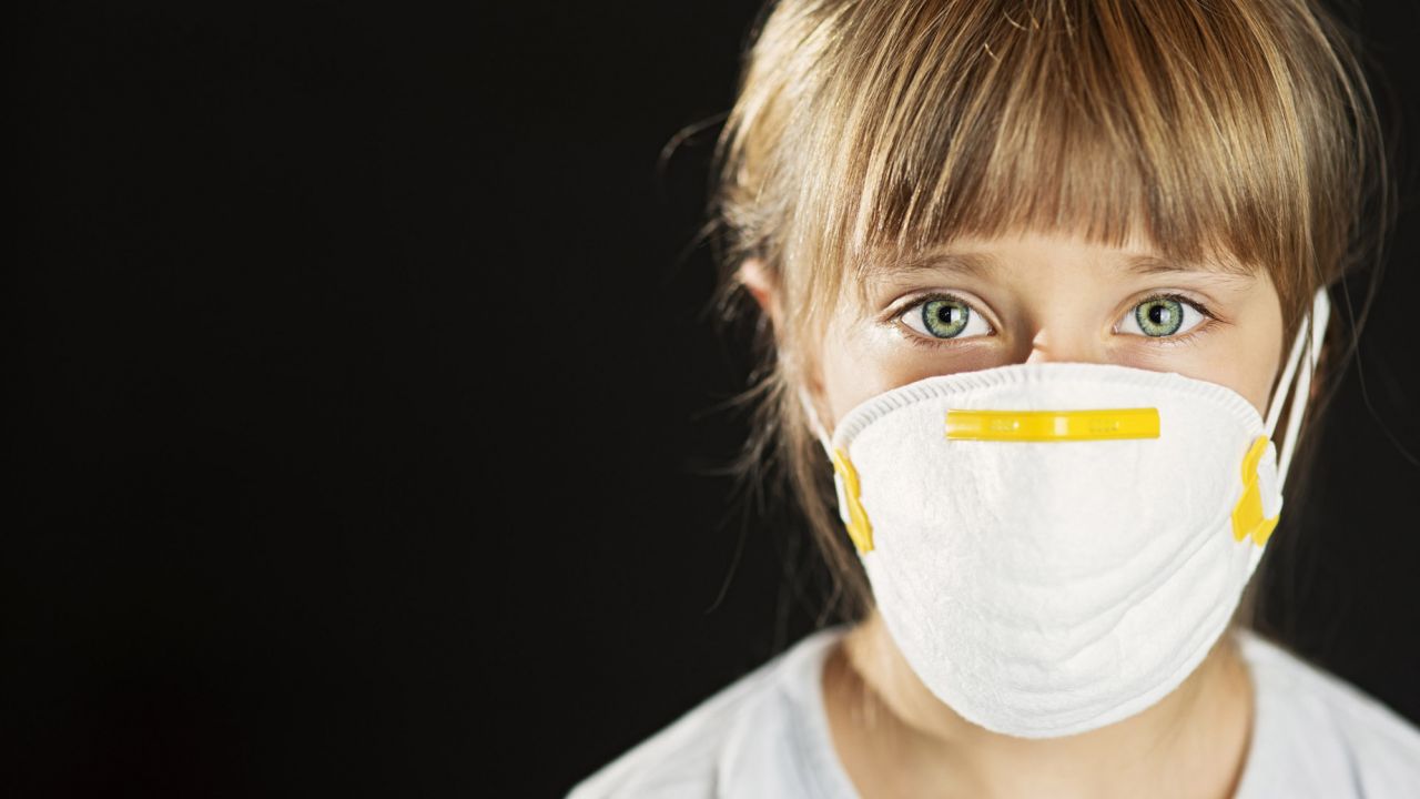 Girl wearing face mask covering nose and mouth facing camera.