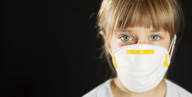 Girl wearing face mask covering nose and mouth facing camera.