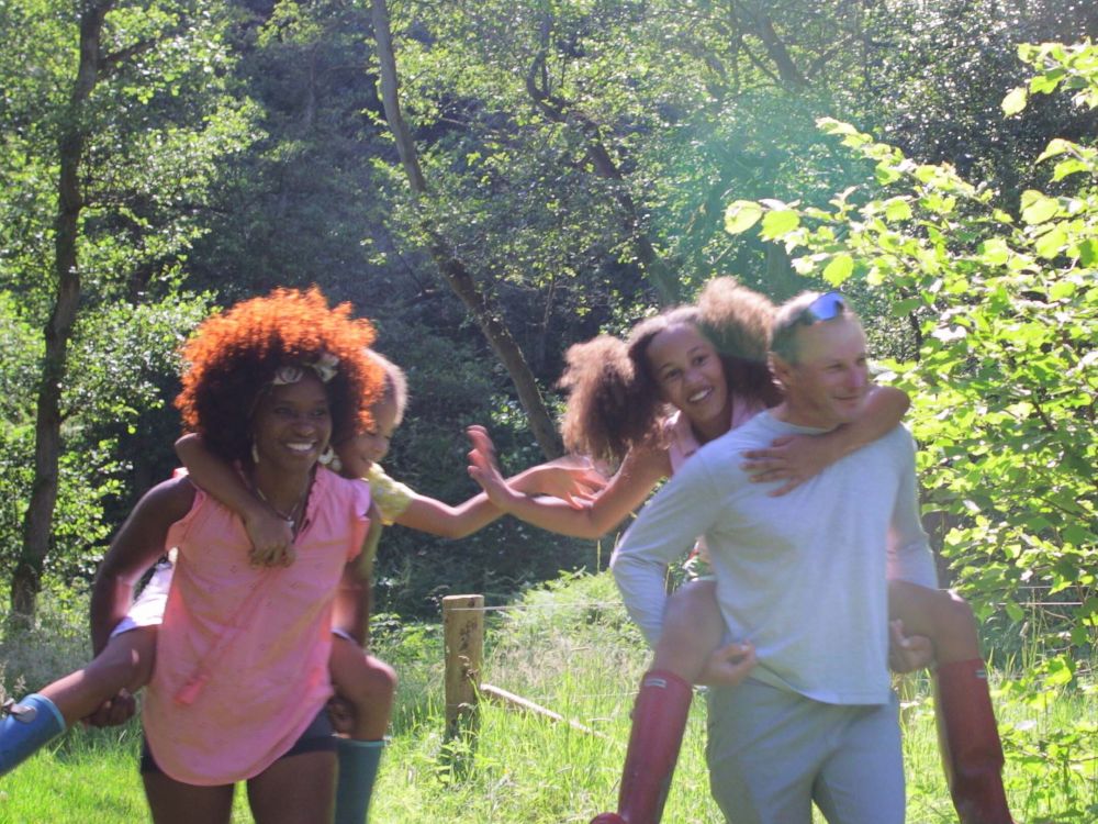 Photo of family of four in a woodland park. Children are having piggy back rides and everyone is smiling.