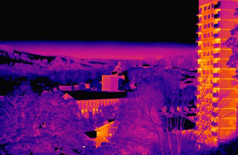 A thermal image showing heat from a terrace of houses and high rise flats amongst cold trees and fields.