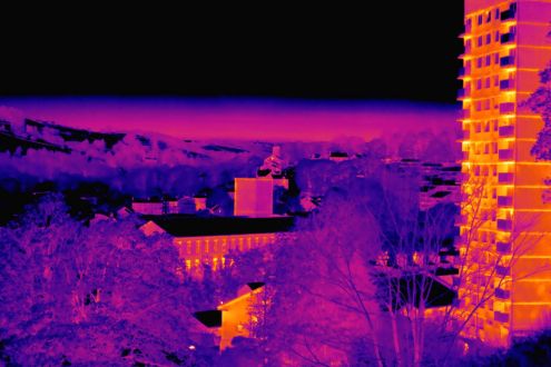 A thermal image showing heat from a terrace of houses and high rise flats amongst cold trees and fields.