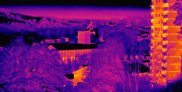 A thermal image showing heat from a terrace of houses and high rise flats amongst cold trees and fields.