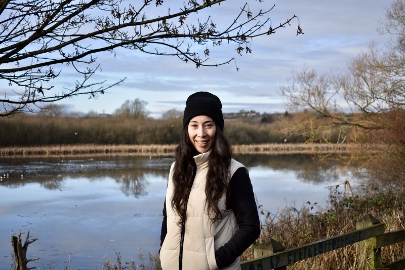 Helen stands by a lake and marsh, smiling.