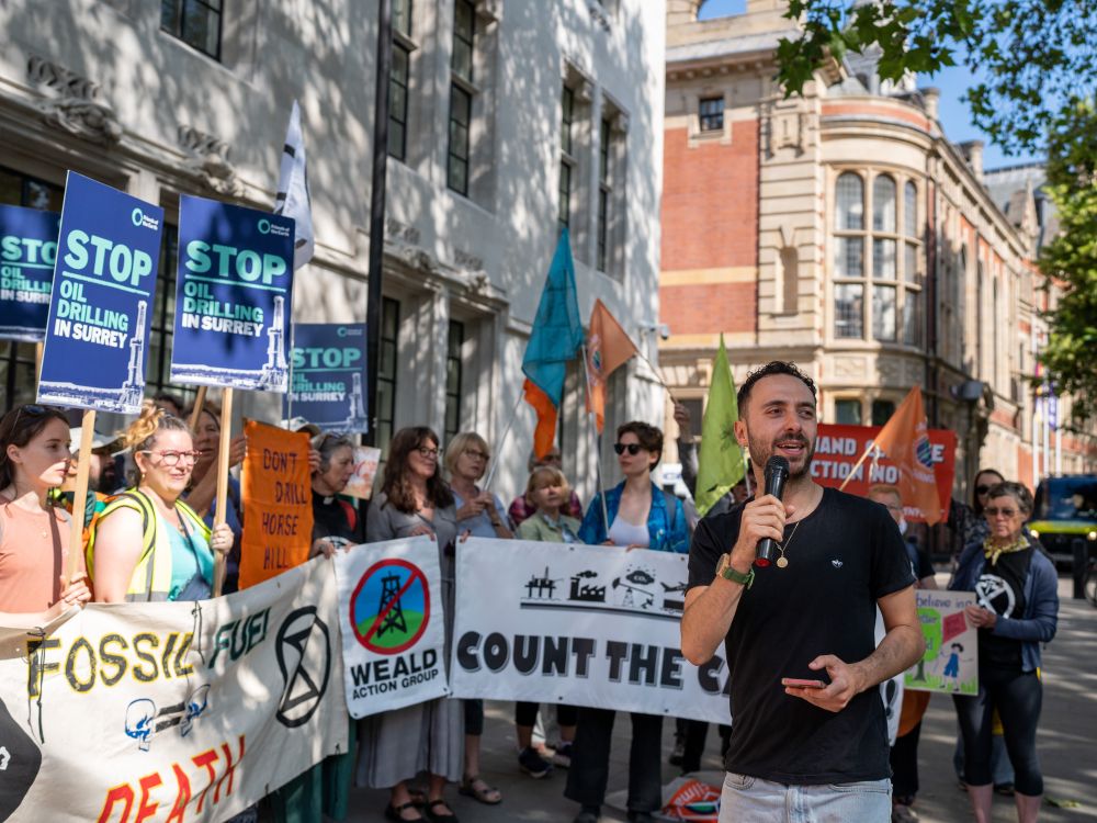A group of people stand on the street with banners and placard, one person speaking into a microphone