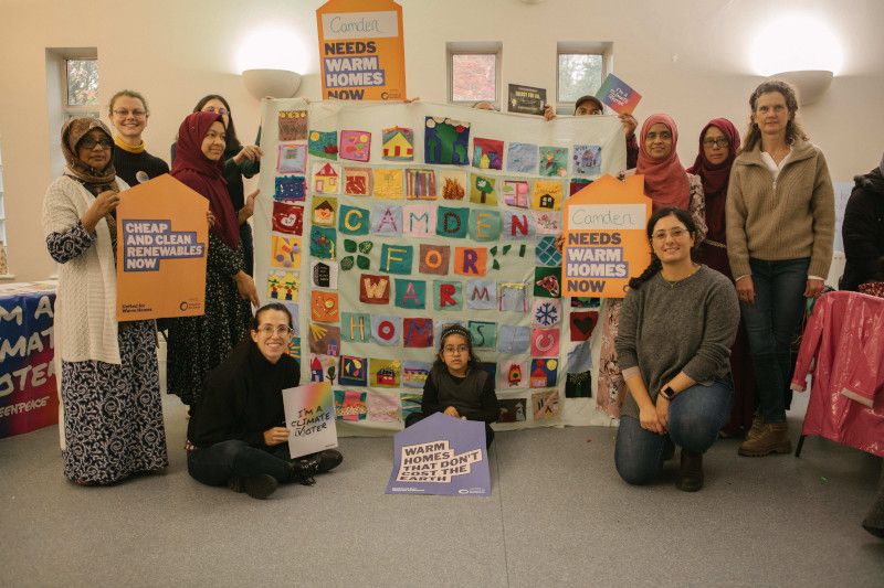 Members of Camden Friends of the Earth proudly holding up their large hand-made quilt with patches related to their communities like homes, trees and hearts. 
