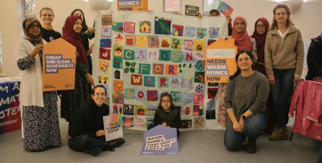 Members of Camden Friends of the Earth proudly holding up their large hand-made quilt with patches related to their communities like homes, trees and hearts. 